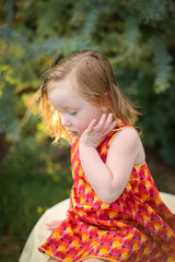 Wall Mural - Portrait of female child wearing bright red dress sitting in natural garden setting