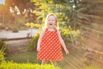 Wall Mural - Little girl wearing red dress exploring garden flooded in golden afternoon light