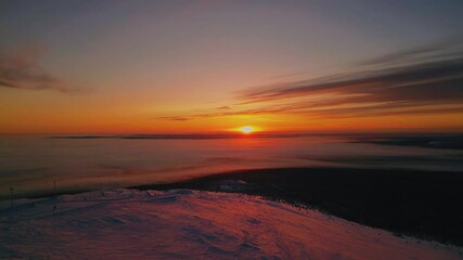 Wall Mural - Aerial drone shot of beautiful sunset over frozen lake in Finland. Warm colors of setting sun reflect on icy surface, creating peaceful winter scene with snow-covered landscape.