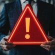 © Preeyanuch - A businessman holds a glowing red warning sign, emphasizing the importance of caution in the workplace or decision-making.