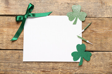 Wall Mural - Blank card with bow, paper clovers and candles on wooden background. St. Patrick's Day celebration