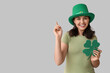 © Pixel-Shot - Beautiful young woman in leprechaun hat with clover pointing at something on grey background. St. Patrick's Day celebration