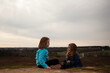 © Cavan Images - Young sisters talking while sitting on hill outdoors