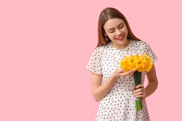 Happy young woman with bouquet of daffodil flowers on pink background