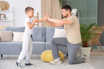 Canvas Print - Young man and his little son boxing in living room