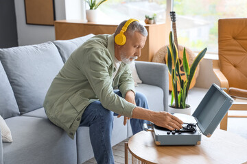 Wall Mural - Mature man in headphones with record player listening to music on sofa at home