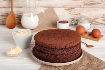 Wall Mural - Delicious chocolate sponge cake cut into layers with ingredients on light wooden background