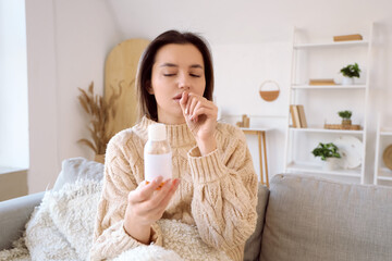 Wall Mural - Sick young woman with cough syrup sitting on sofa at home