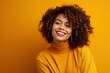 © nsit0108 - Studio portrait of cheerful young woman with curly hair and toothy smile wearing yellow turtleneck and jacket, posing against yellow background