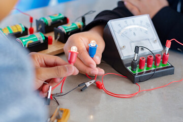 Children are studying electrical circuit systems by experimenting with electrical connections using a small electric meter and a small flashlight bulb in physics science class, soft focus.