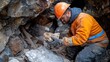© Khaisan - A man in an orange work jacket and helmet examines a rock sample in a mine