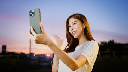 A cheerful woman taking selfie outdoors during sunset, with vibrant sky in background, expressing joy and positivity. businesswoman digital lifestyle