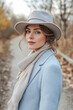 © wernerimages - A stylish woman in a light blue coat and scarf walks along a serene path in nature, embodying tranquility, contemporary fashion, and a connection to her surroundings.