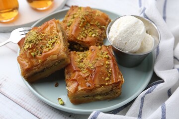 Delicious baklava with crushed nuts and ice cream on light wooden table, closeup