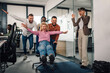 © Zamrznuti tonovi - Business colleagues pushing businesswoman on office chair, having fun at work
