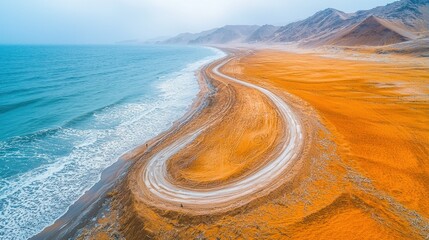 Wall Mural - Coastal desert road curves by ocean, hazy mountains backdrop, aerial view.