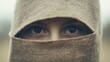 © musa - Close-up of woman's eyes peeking through burlap cloth.