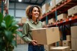 © miss irine - Businesswoman happily prepares shipping orders in warehouse. Small business owner packages products for delivery. Holds cardboard box. Plenty of boxes stacked high in warehouse storage area. Modern