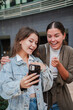 © Jose Calsina - Excited Young Women Sharing Joyful Moments While Viewing Content on a Smartphone in a Cheerful Outdoor Setting, Capturing Their Genuine Reactions and Expressions of Delight with a Cellphone in Hand