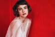 © callisto - Model poses in a minimalist white outfit against a vivid red backdrop in a studio setting during a fashion shoot