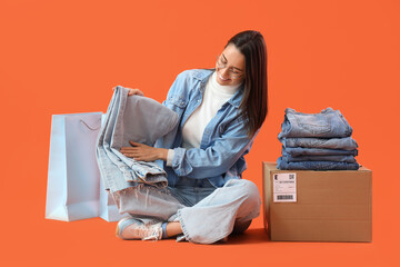 Wall Mural - Female seller with jeans and shopping bags on orange background