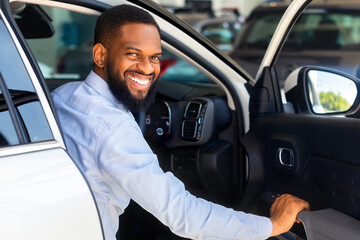 Wall Mural - Happy African American Man Getting In Luxury Car And Smiling At Camera, Cheerful Black Male Opening Door Of His New Automobile In Dealership Center, Enjoying Characteristics Of Vehicle, Closeup