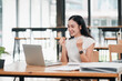 © Satori Studio - A joyful young woman in a modern office celebrates a successful achievement while working on her laptop.