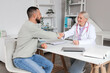 © Pixel-Shot - Female doctor with young man shaking hands at table in clinic