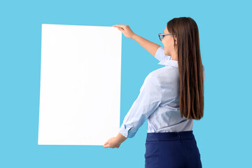 Wall Mural - Pretty young businesswoman with blank poster on blue background, back view