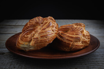 A clay plate with two profiteroles stands on a wooden surface. Profiterole cake. Eclair in the shape of a ring.