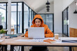 © David - Young asian woman wearing orange shirt hold use laptop pc computer drink coffee sit alone at table in coffee shop cafe restaurant indoors work or study. Freelance mobile office business concept