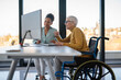 © NDABCREATIVITY - Disabled woman in wheelchair looking at computer, discussing startup project with interracial team