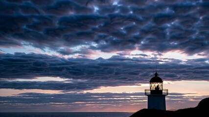 Fototapete - Stunning sunset illuminates clouds behind a lighthouse by the ocean