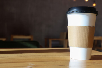 Wall Mural - Blank take away craft paper cup of coffee on wooden table with blurred cafe background for copy space of mock up