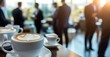© David Giraud - Une réunion professionnelle avec des tasses de café sur un table, arrière-plan flou avec des gens en costume debout, un espace de bureau avec de grandes fenêtres donnant sur l'extérieur.