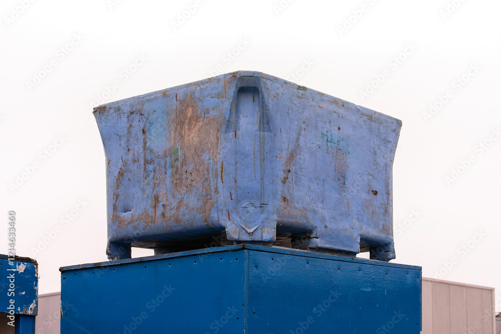 weathered plastic bio waste bin stands outside on a blue wooden box