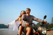 © artiemedvedev - Couple rides motorbike by beach. Woman enjoys freedom, open arms. Guy controls motorcycle. Sunny day, ocean, vacation vibes. Romantic adventure, explore exotic coast, bike. Bonding.