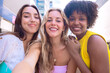 © alfons - Three happy young women taking a selfie together in a city street