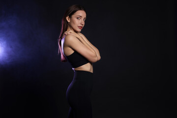 Wall Mural - Beautiful woman in stylish sportswear on dark background with color light and smoke. Space for text