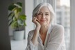 © Sena - A smiling mature woman with short gray hair sits by a window, looking peaceful and content.