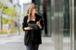 © ultramansk - Confident businesswoman walking through a modern urban environment with reflective glass buildings, holding a tablet. A dynamic and empowering portrayal of contemporary professional life.
