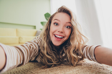 Joyful young woman with blond hair relaxing indoors, enjoying leisure time on a sunny day in modern living room, wearing casual striped pullover, capturing her cheerful smile and carefree charm.