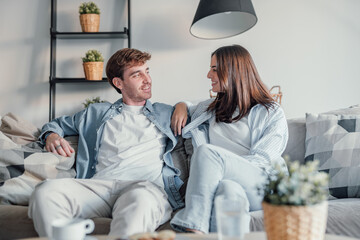 Young happy couple having fun talking laughing relaxing at home on couch, boyfriend embracing girlfriend telling funny joke sitting on sofa, humor in relationships, enjoying weekend together.