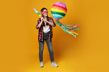 Woman with tied eyes breaking pinata on orange background