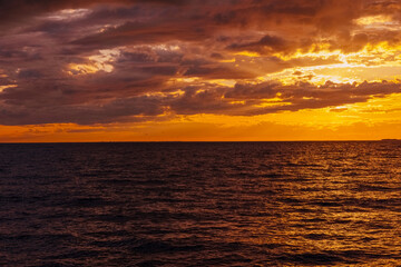 Wall Mural - the water surface of the sea under a cloudy sky, illuminated by the rays of the setting sun at sunset