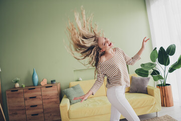 Wall Mural - Young woman joyfully dancing in bright living room with stylish decor, expressing happiness and freedom on a relaxing weekend at home, wearing a striped pullover and enjoying daylight indoors.