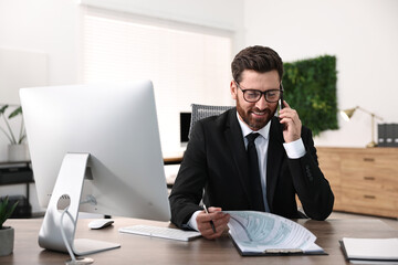 Wall Mural - Man talking on smartphone while working at table in office