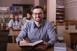 © New Africa - Portrait of smiling man with book at desk in public library