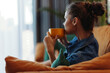 © SHOTPRIME STUDIO - A woman sitting on a couch with a cup of coffee, looking out the window in contemplation