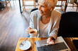 © Davor - Senior businesswoman enjoying coffee while working on laptop at cafe